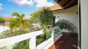 Een balkon met een witte balustrade, een pannendak en verschillende groene planten.