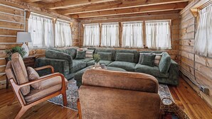 Interior de una cabaña de troncos con un sofá verde, una silla de madera y una lámpara.