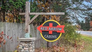 Un letrero de Red Arrow Cabins, con una valla de madera y un muro de piedra al fondo.