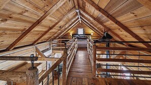 Un dormitorio en el ático con piso de madera, una escalera central, una cama y una ventana.