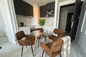 Una cocina moderna con armarios oscuros, un microondas y una mesa de vidrio rodeada de sillas marrones.