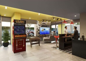 A lobby with a Pac-Man arcade game, a large flat-screen TV, a reception desk, and a seating area with a patterned rug. - Ñuñoa - Edificio New Egaña by Domus (Santiago)