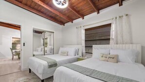 Une chambre avec deux lits, un miroir, une fenêtre avec des stores et un plafond en bois.