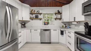 Une cuisine moderne avec des armoires blanches, des appareils en acier inoxydable et des poutres en bois au plafond.