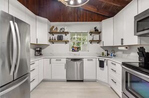 Eine moderne Küche mit weißen Schränken, Edelstahlgeräten und Holzbalkendecke.