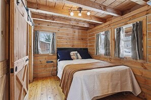 A wooden cabin bedroom with a bed, curtains, and a ceiling light fixture.