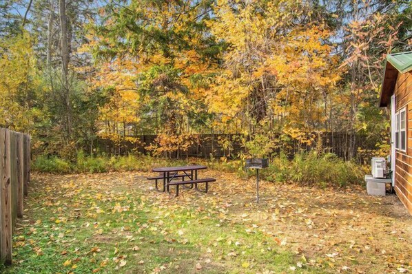 A wooden cabin with a picnic table and mailbox in a wooded area.