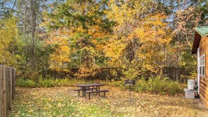 A wooden cabin with a picnic table and mailbox in a wooded area.