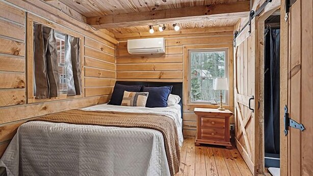 A wooden cabin bedroom with a bed, bedside table, and a window.