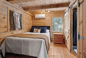Quarto de cabana de madeira com cama, mesa de cabeceira e uma janela.