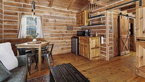 A log cabin interior with a dining area, kitchen, and a sliding door leading to another room. - The Hideout Cabin | Firepit | Nature | Dunes (Sawyer)