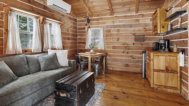 A log cabin interior with a sofa, dining table, chairs, a coffee maker, and a small kitchen area. - The Hideout Cabin | Firepit | Nature | Dunes (Sawyer)