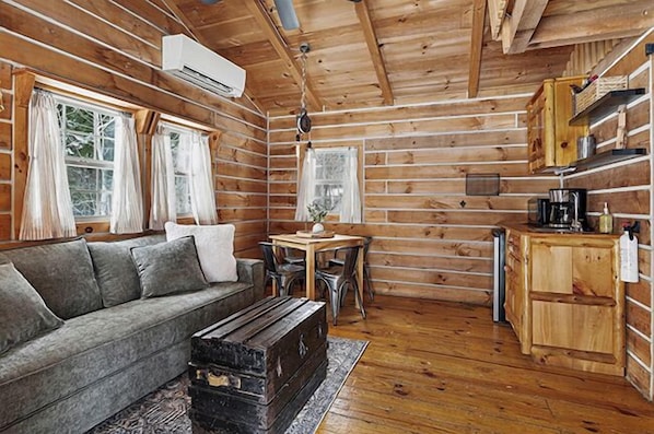 A log cabin interior with a sofa, dining table, chairs, a coffee maker, and a small kitchen area.