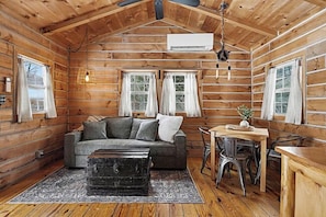 A log cabin interior with a sofa, dining table, chairs, and a small table with a plant.