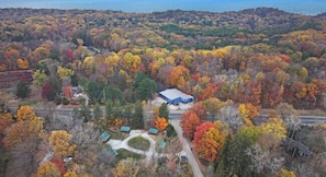 An aerial view of a property with a blue-roofed building surrounded by autumn-colored trees.