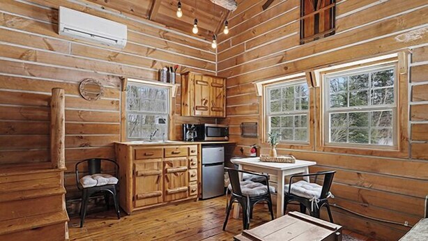 Interior de una cabaña de troncos con cocina, comedor y una pequeña mesa.