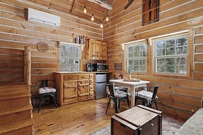 Interior de una cabaña de troncos con cocina, comedor y una pequeña mesa.