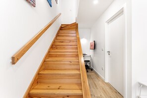 Eine Holztreppe mit Handlauf, eine weiße Tür und ein Schreibtisch mit Stuhl in einem Flur.