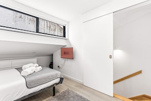Ein modernes Hotelzimmer mit Bett, Fernseher, Kleiderschrank und kleinem Schreibtisch.