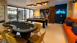 Een pooltafel met stoelen, een bank en een neonreclame in een modern ingerichte ruimte.