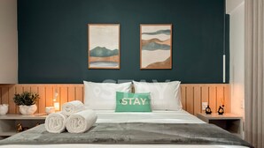 Een hotelkamer met een bed, kussens, een bordje 'STAY' en twee ingelijste kunstwerken aan de muur.