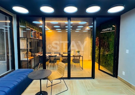 A modern interior with a meeting room, a seating area with a table and chairs, and a glass wall with a 'meeting' sign.