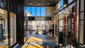 Een sportschool met trainingsapparatuur, grote ramen en een uitzicht op gebouwen.
