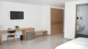 Een moderne hotelkamer met een bed, een bureau met stoel, een kleine prullenbak, een televisie en een houten garderobekast.