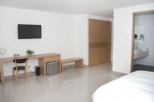 Una habitación de hotel moderna con cama, escritorio con silla, un pequeño cubo de basura, televisor y armario de madera.