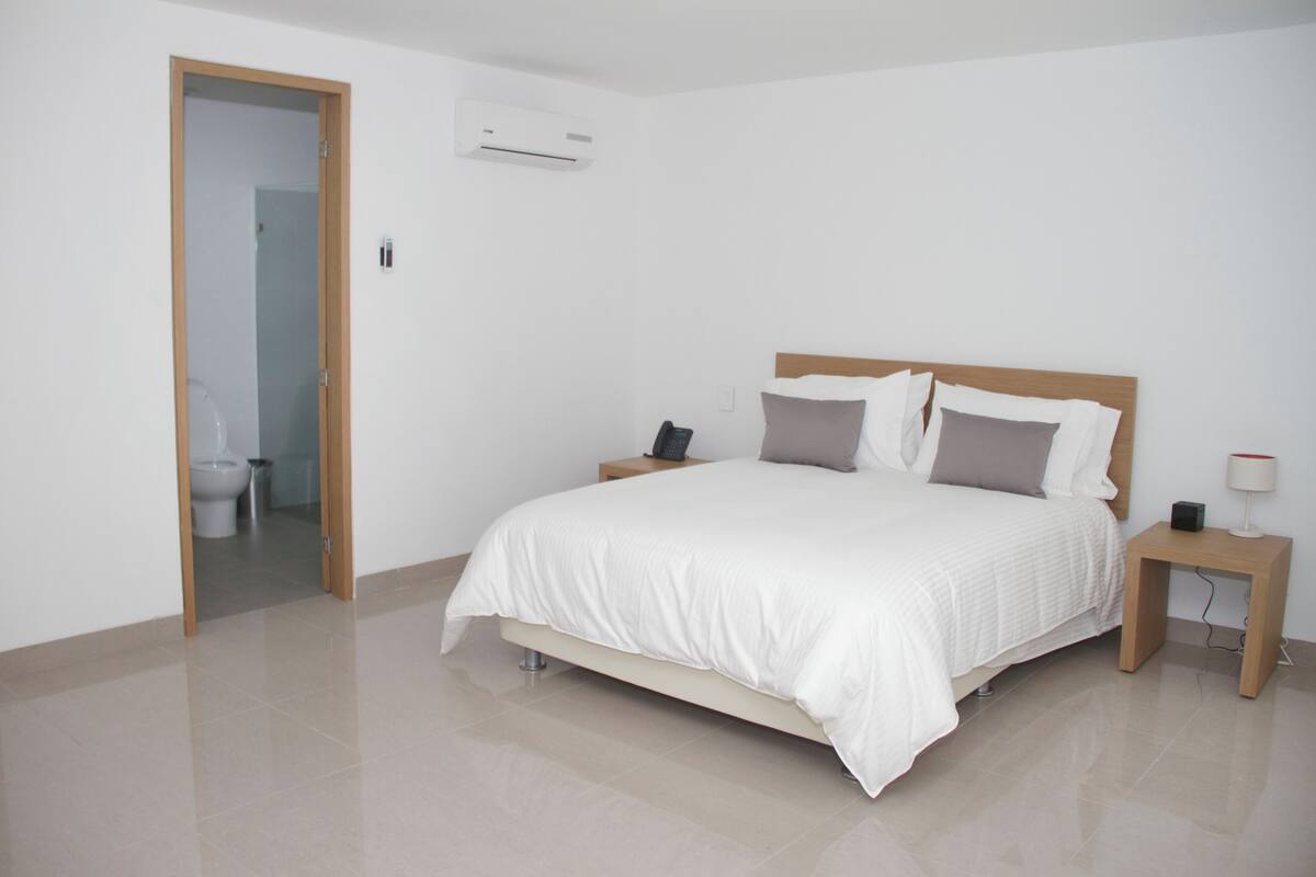 Un dormitorio con cama, mesitas de noche, aire acondicionado y puerta de baño.