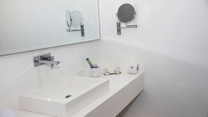 Een moderne badkamer met een wit wastafel, twee spiegels en toiletartikelen op het aanrecht.