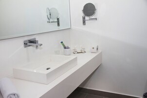Un baño moderno con un lavabo blanco, dos espejos y artículos de aseo en la encimera.