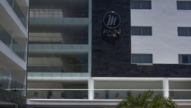 Een modern hotel met een opvallend 'Malibu Hotel' bord, een ruime entree en een verzorgd buitengebied met plantenbakken.