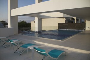 Piscina en la azotea con sillones de descanso, cielo despejado y arquitectura moderna.
