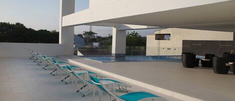 A poolside area with lounge chairs, a pool, and a modern building structure.