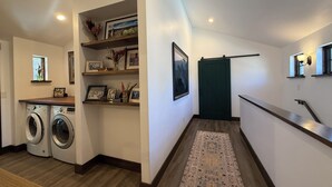 A laundry area with a washing machine and dryer, a wooden bench, a rug, and a green door. - 3BR Farmhouse in Durango with Fitness Room, Sauna, Bidets, Theater Entertainment (Durango)
