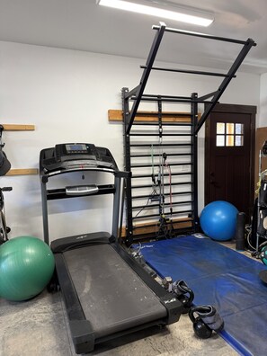 Une salle de sport à domicile équipée d’un tapis de course, d’un ballon d’exercice, d’un kettlebell et d’une structure pour faire de la traction.