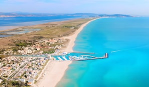 Vue aérienne d’une zone côtière comprenant un port de plaisance, une plage de sable et des immeubles résidentiels.