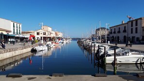 Un puerto deportivo con barcos amarrados, un paseo marítimo y edificios con tiendas y cafés.