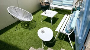 Un patio con una silla blanca, una mesita, un banco con cojines a rayas y una planta en maceta.