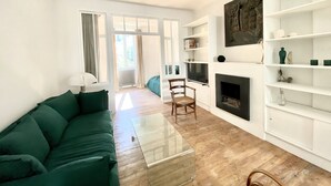 Una sala de estar con un sofá verde, una mesa de centro de vidrio, una chimenea y estanterías blancas.