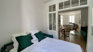 Un dormitorio con una cama, almohadillas verdes, suelo de madera y un área de comedor con sillas y una mesa.