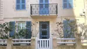 Un edificio con una verja blanca, contraventanas azules y un balcón con ornamentación de hierro.