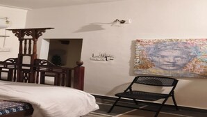 Een slaapkamer met een bed, een houten stoel, een wandplank en een groot abstract schilderij.