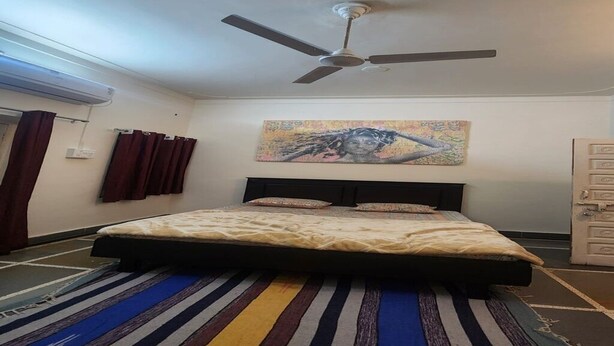 Een slaapkamer met een bed, een plafondventilator, een kleurrijk tapijt en een schilderij aan de muur.