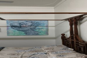 A bedroom with a bed, a wooden headboard, and a wall-mounted painting. - ROYAL REST AWAIT  ON RING ROAD UDAIPUR (Gordhan Vilas Rural)