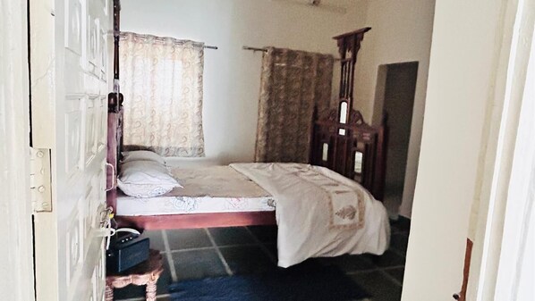 A bedroom with a bed, curtains, a wooden wardrobe, and a small table. - ROYAL REST AWAIT  ON RING ROAD UDAIPUR (Gordhan Vilas Rural)