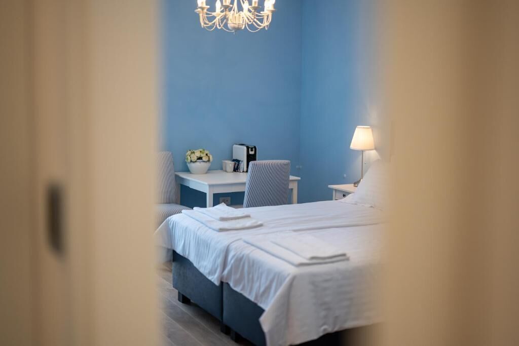 A hotel room with a bed, a desk, a chair, a lamp, and a chandelier.