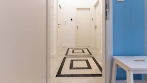 Käytävä, jossa on geometrisesti kuvioitu lattia, valkoiset ovet ja sininen korosteseinä.