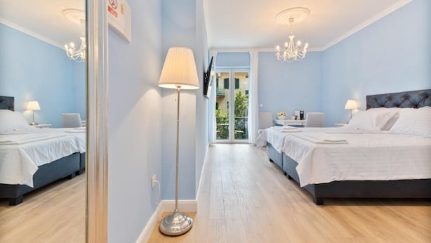 Hotellihuone, jossa on kaksi sänkyä, lattiavalaisin, kattokruunu ja näkymä lasiovesta.
